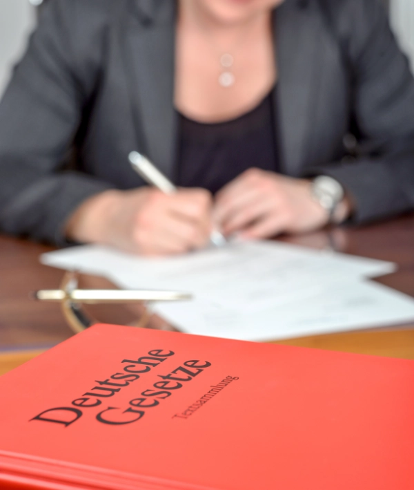 Symbolbild: Eine Frau füllt ein Formular aus und vor ihr liegt ein Buch mit dem Titel